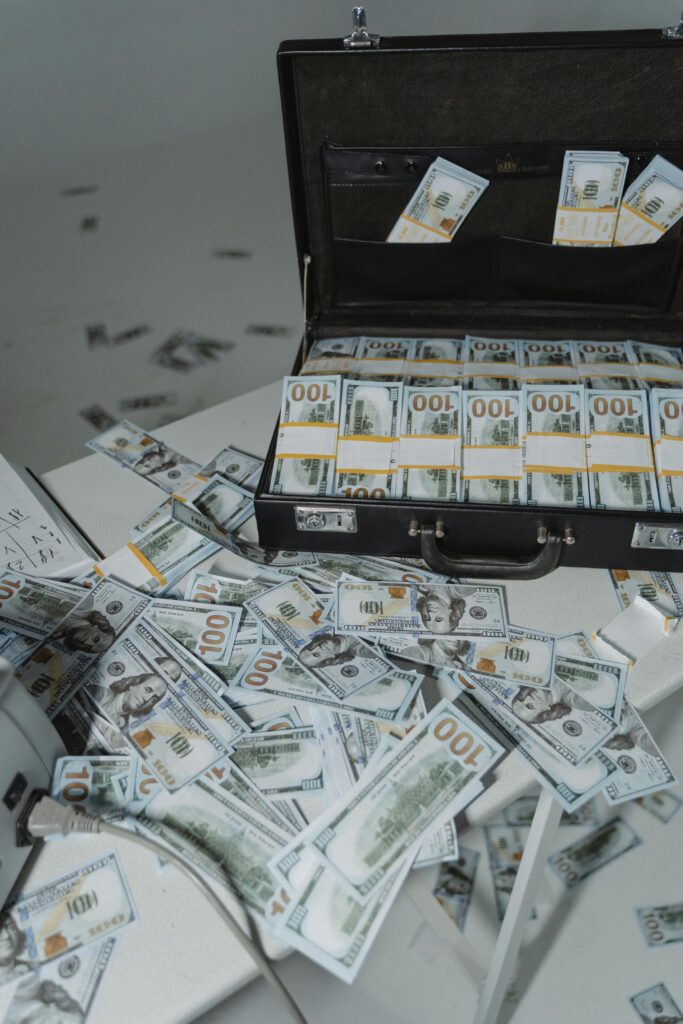 A briefcase overflowing with neatly stacked US dollar bills surrounded by scattered currency on a table.