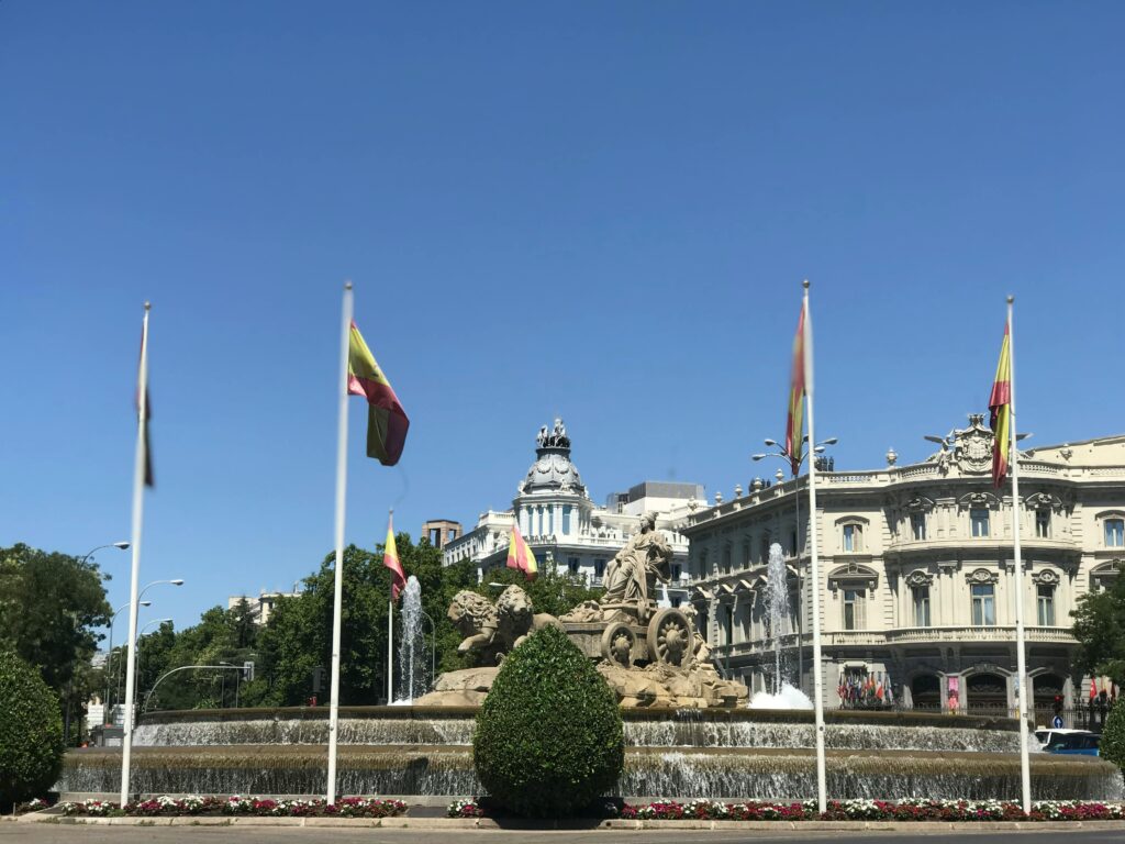 Beautiful view of Cibeles Fountain with Spanish flags under a clear blue sky in Madrid, Spain.